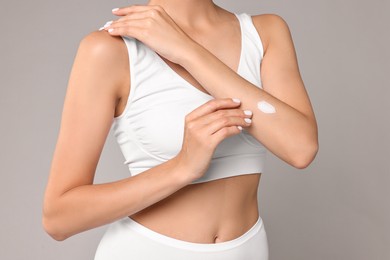 Woman applying cream onto hand on grey background, closeup. Body care