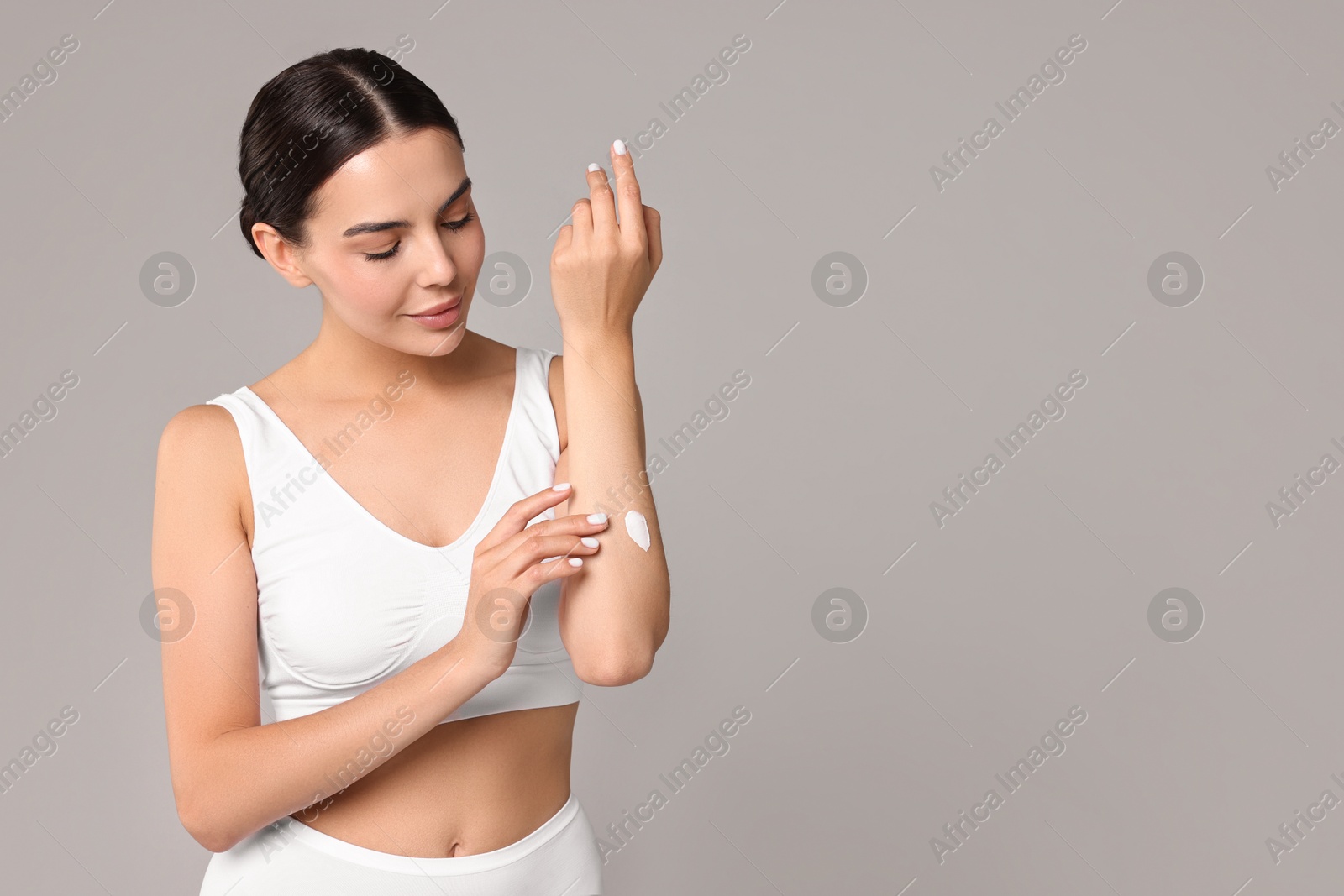 Photo of Beautiful woman applying cream onto hand on grey background, space for text. Body care