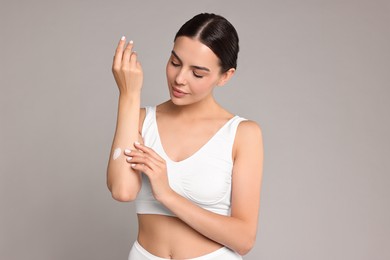 Photo of Beautiful woman applying cream onto hand on grey background. Body care