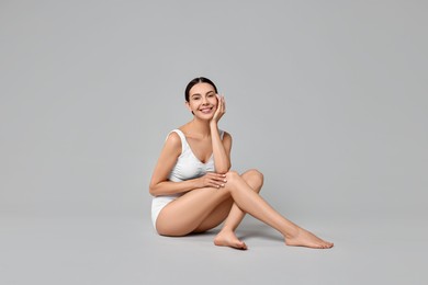 Smiling woman with perfect skin in underwear on grey background. Body care