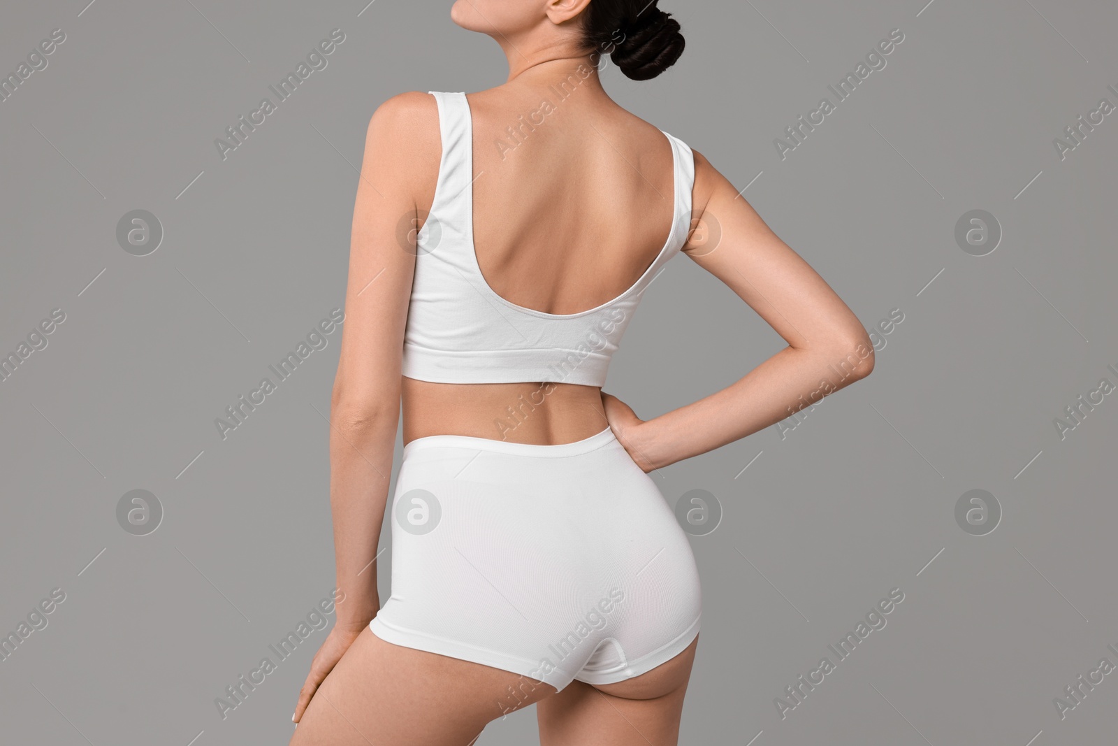 Photo of Woman with perfect skin in underwear on grey background, back view. Body care