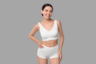 Photo of Smiling woman with perfect skin in underwear on grey background. Body care