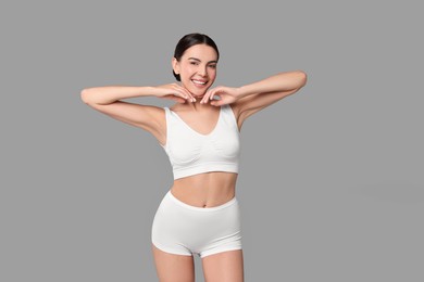 Photo of Smiling woman with perfect skin in underwear on grey background. Body care