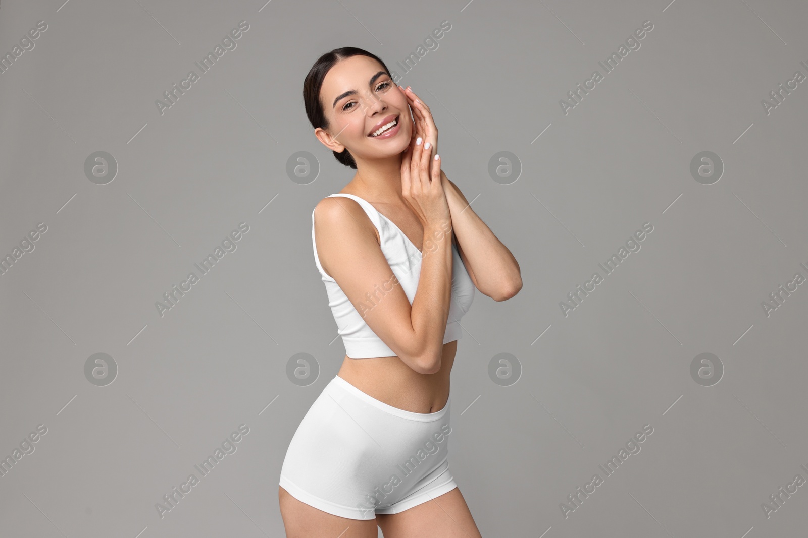 Photo of Smiling woman with perfect skin in underwear on grey background. Body care