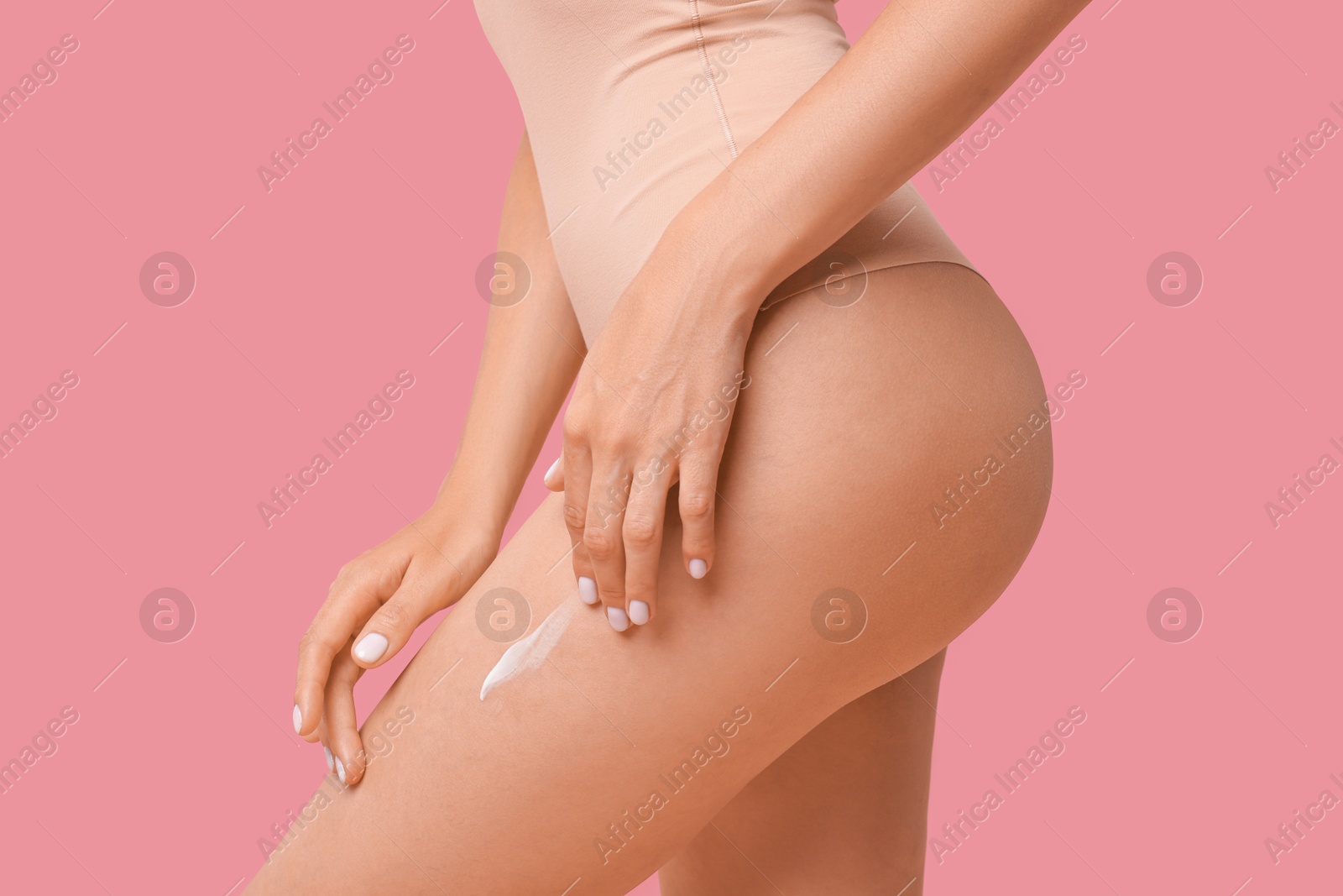 Photo of Woman applying cream onto leg on pink background, closeup. Body care