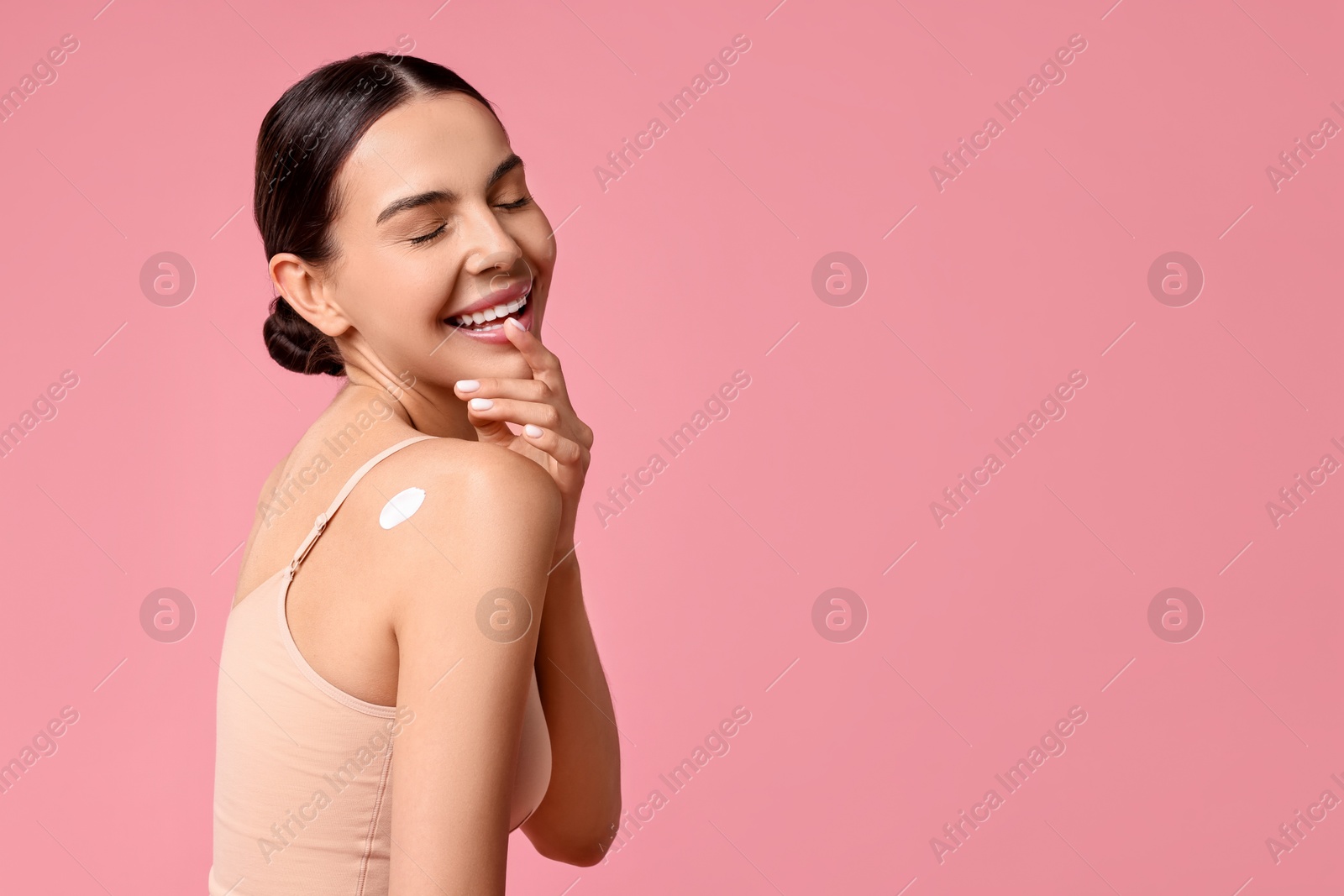 Photo of Smiling woman with cream on shoulder against pink background, space for text. Body care