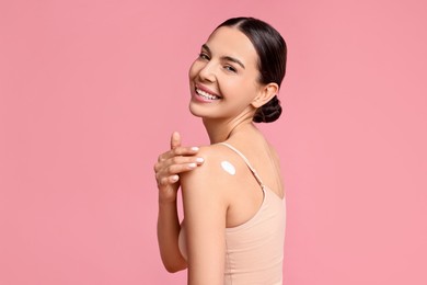 Photo of Smiling woman with cream on shoulder against pink background. Body care