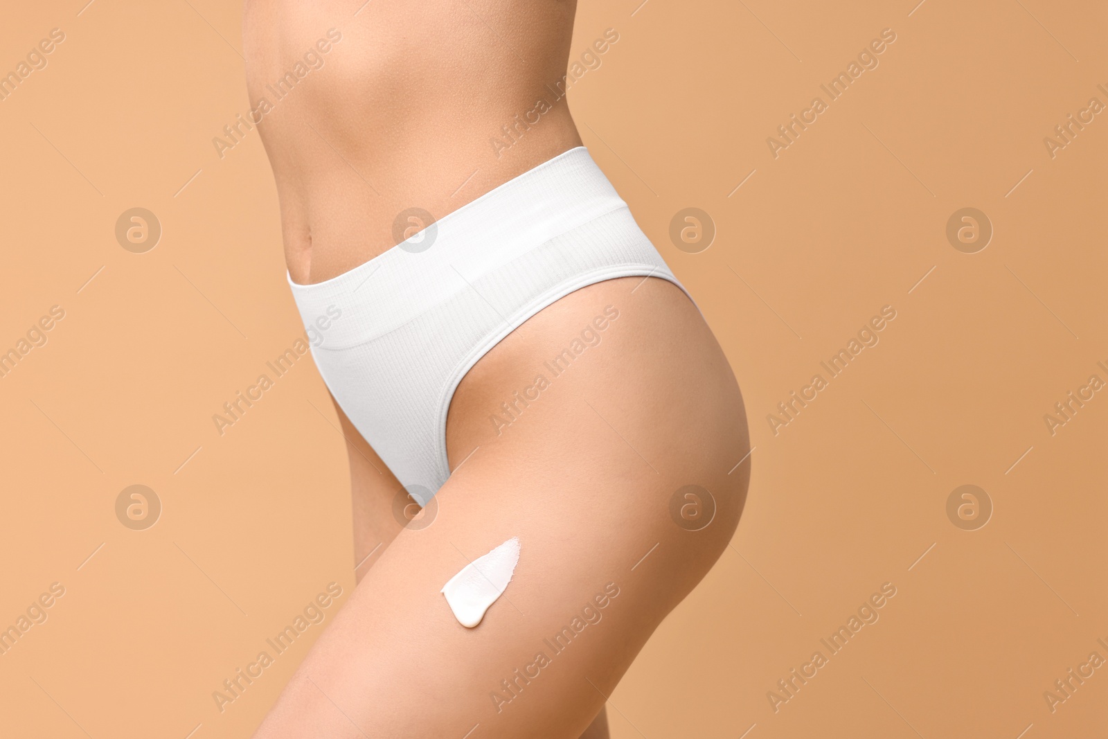 Photo of Woman with cream on hip against beige background, closeup. Body care