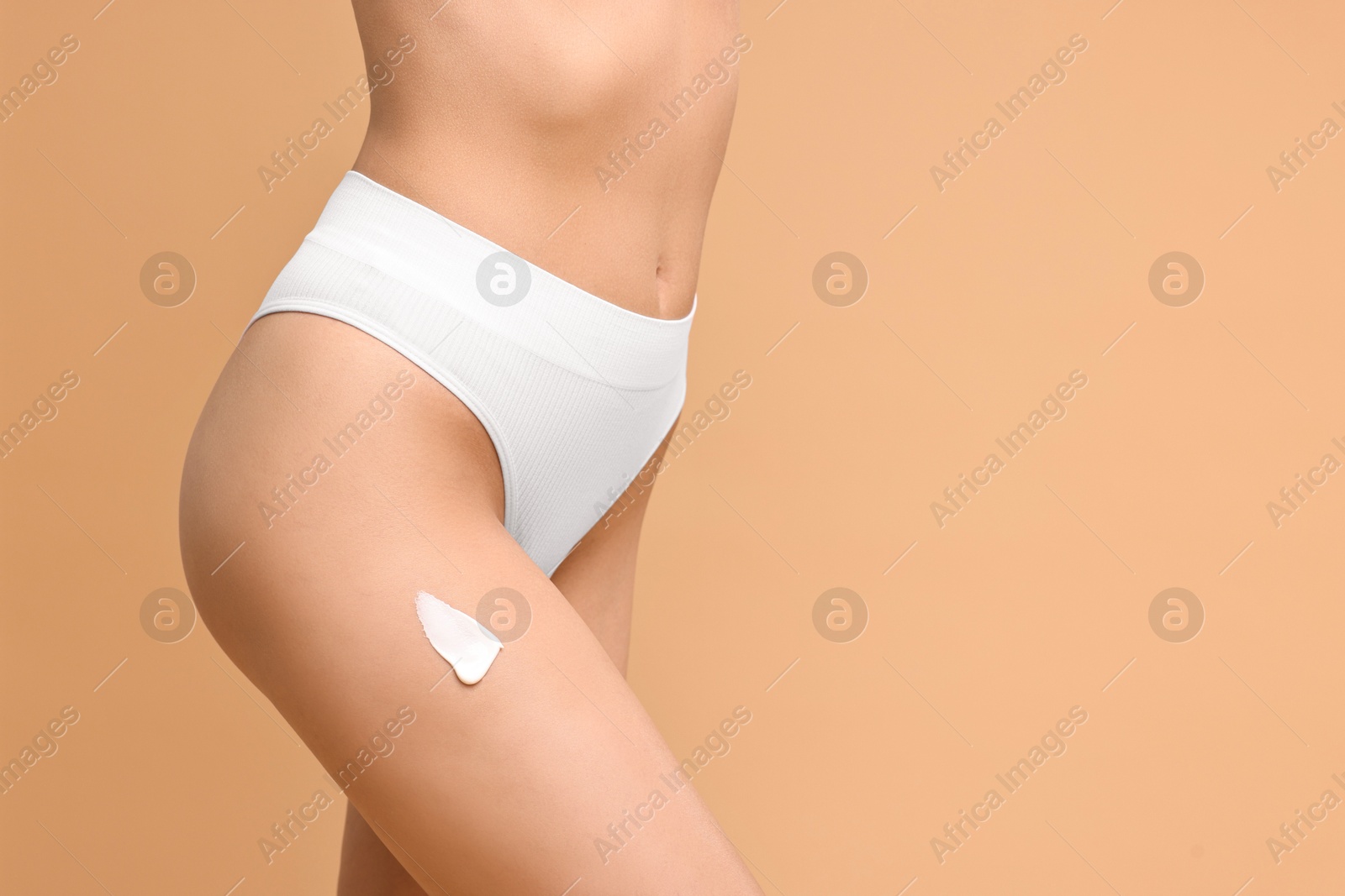 Photo of Woman with cream on hip against beige background, closeup and space for text. Body care