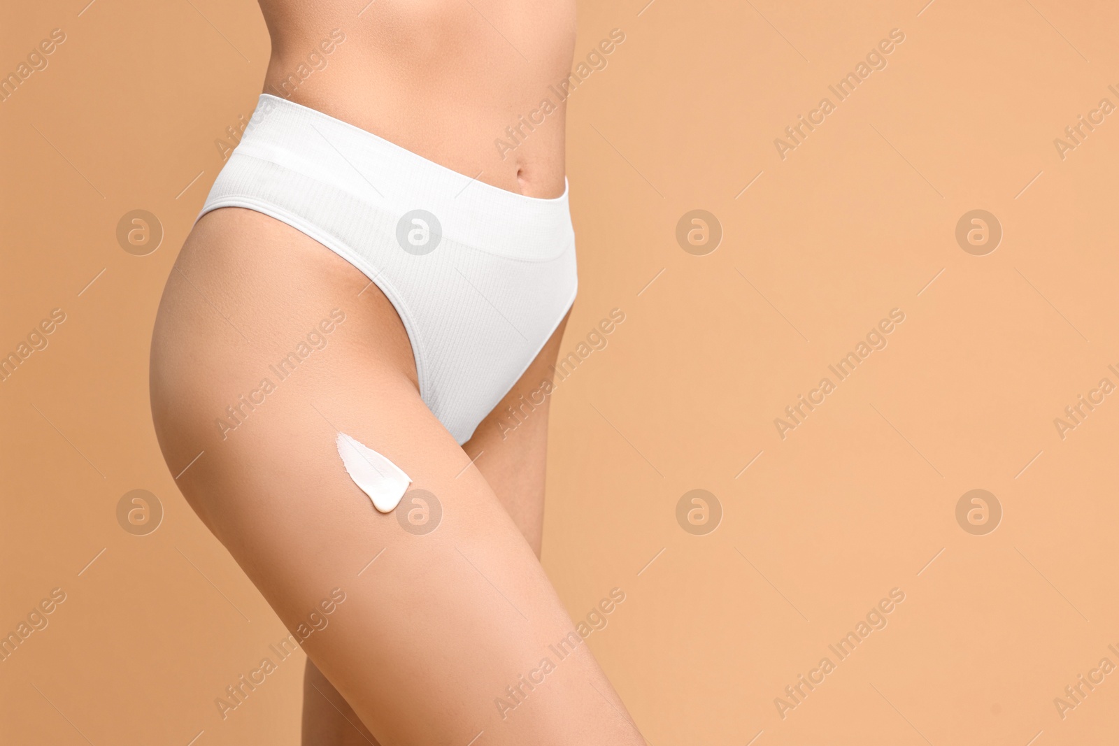 Photo of Woman with cream on hip against beige background, closeup and space for text. Body care