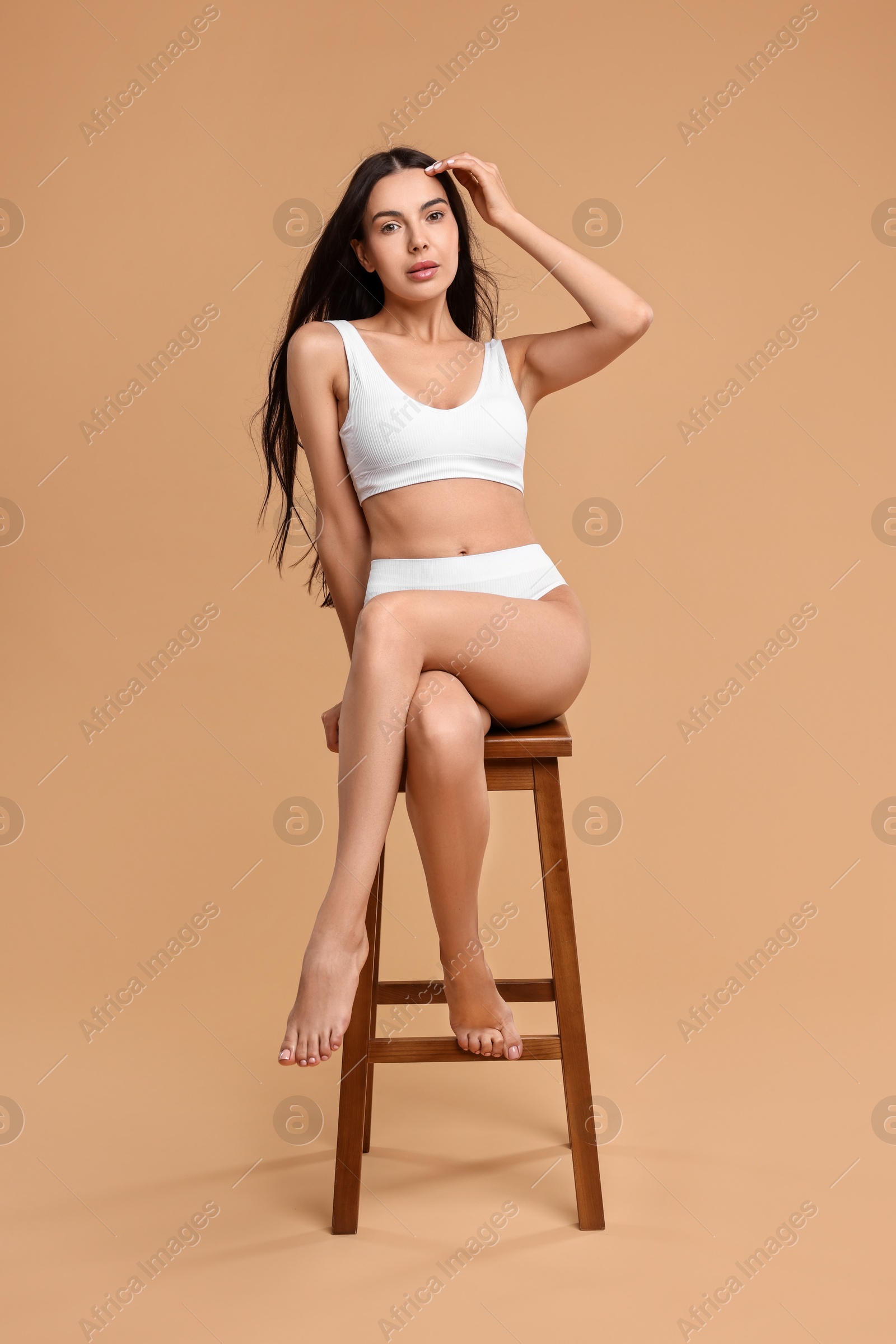 Photo of Beautiful woman with perfect skin in underwear posing on stool against beige background. Body care