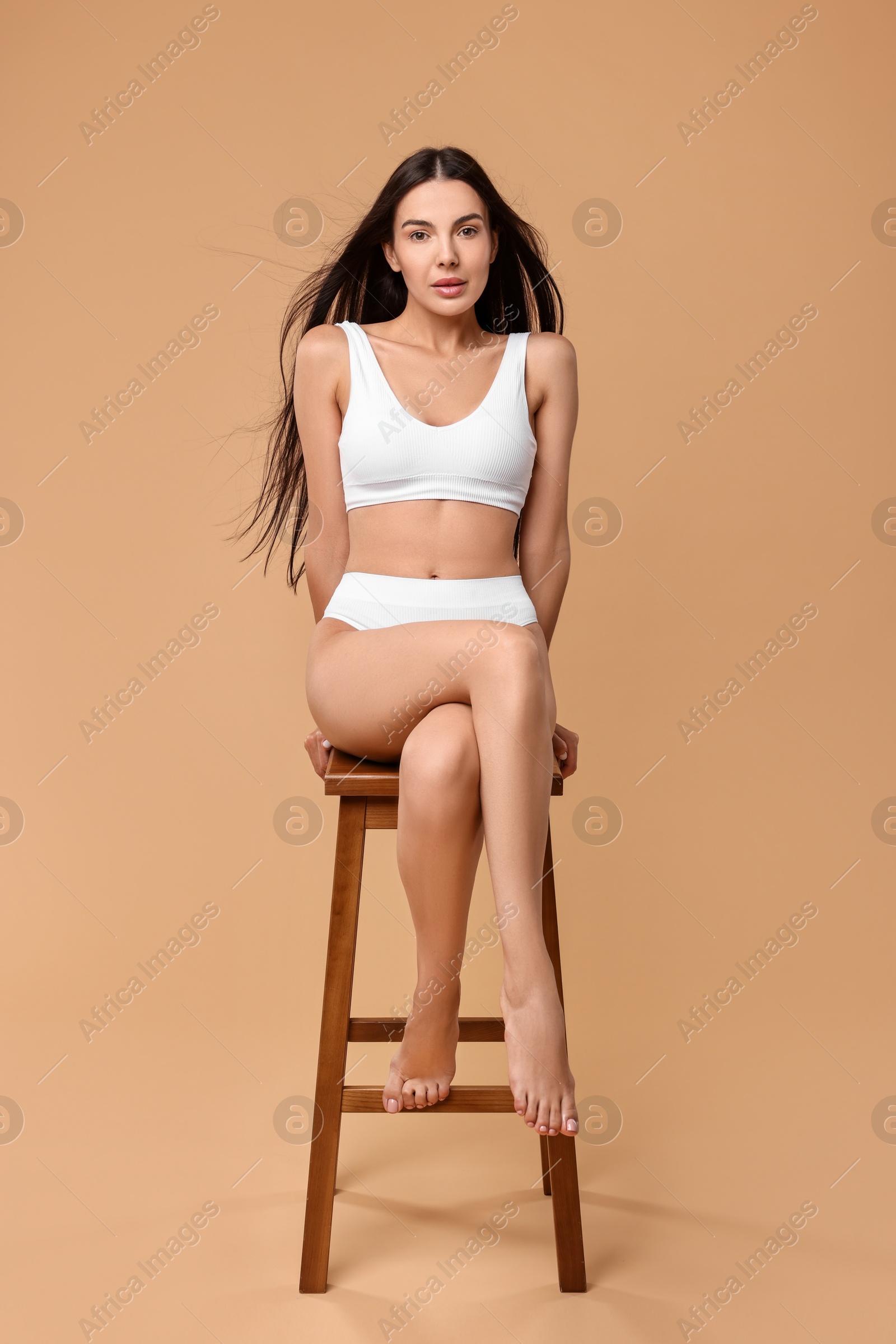 Photo of Beautiful woman with perfect skin in underwear posing on stool against beige background. Body care