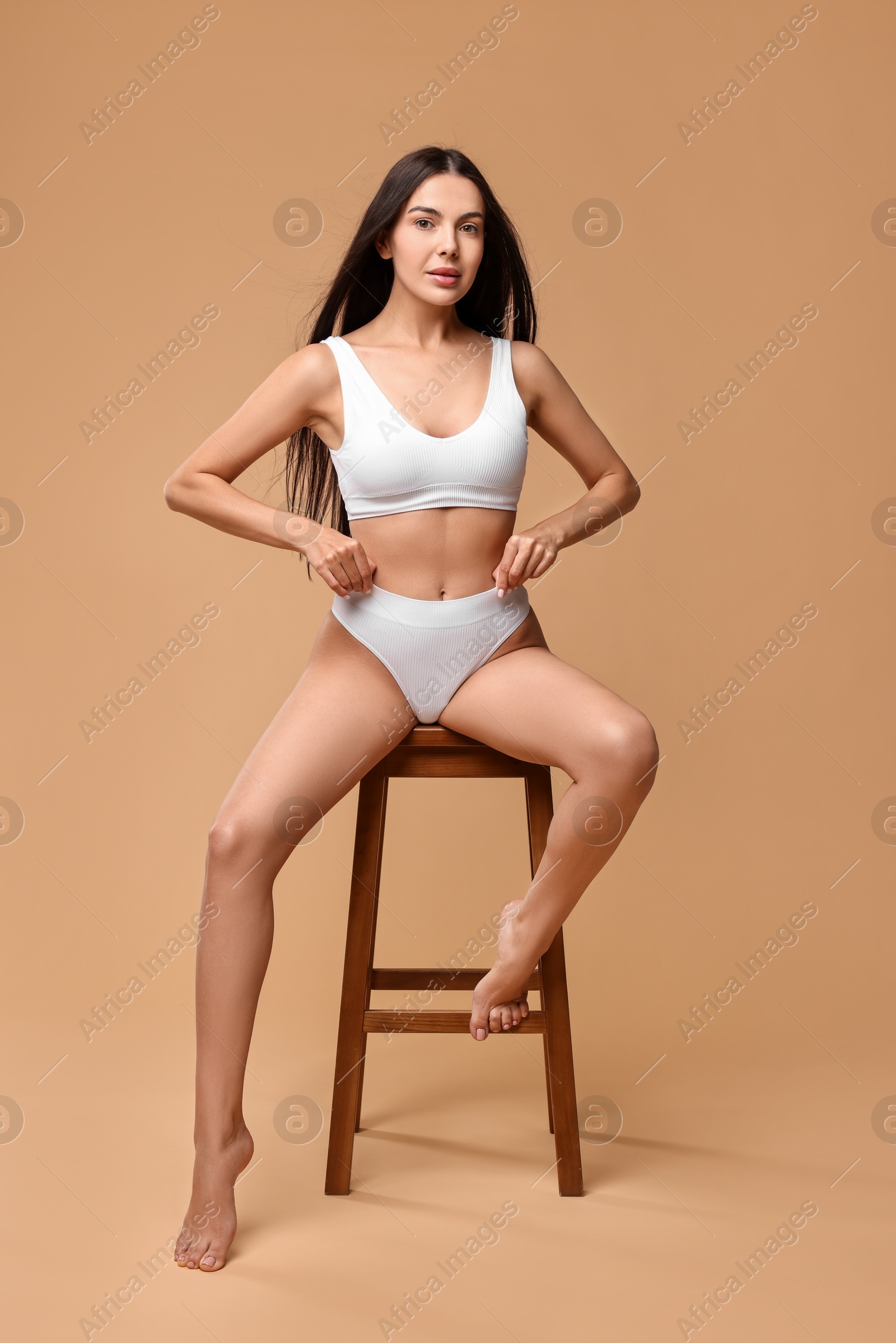 Photo of Beautiful woman with perfect skin in underwear posing on stool against beige background. Body care