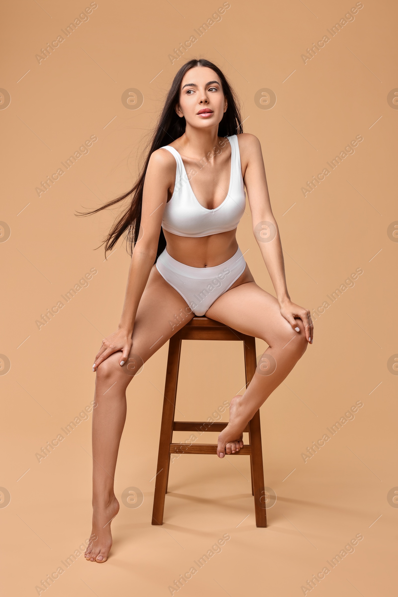 Photo of Beautiful woman with perfect skin in underwear posing on stool against beige background. Body care