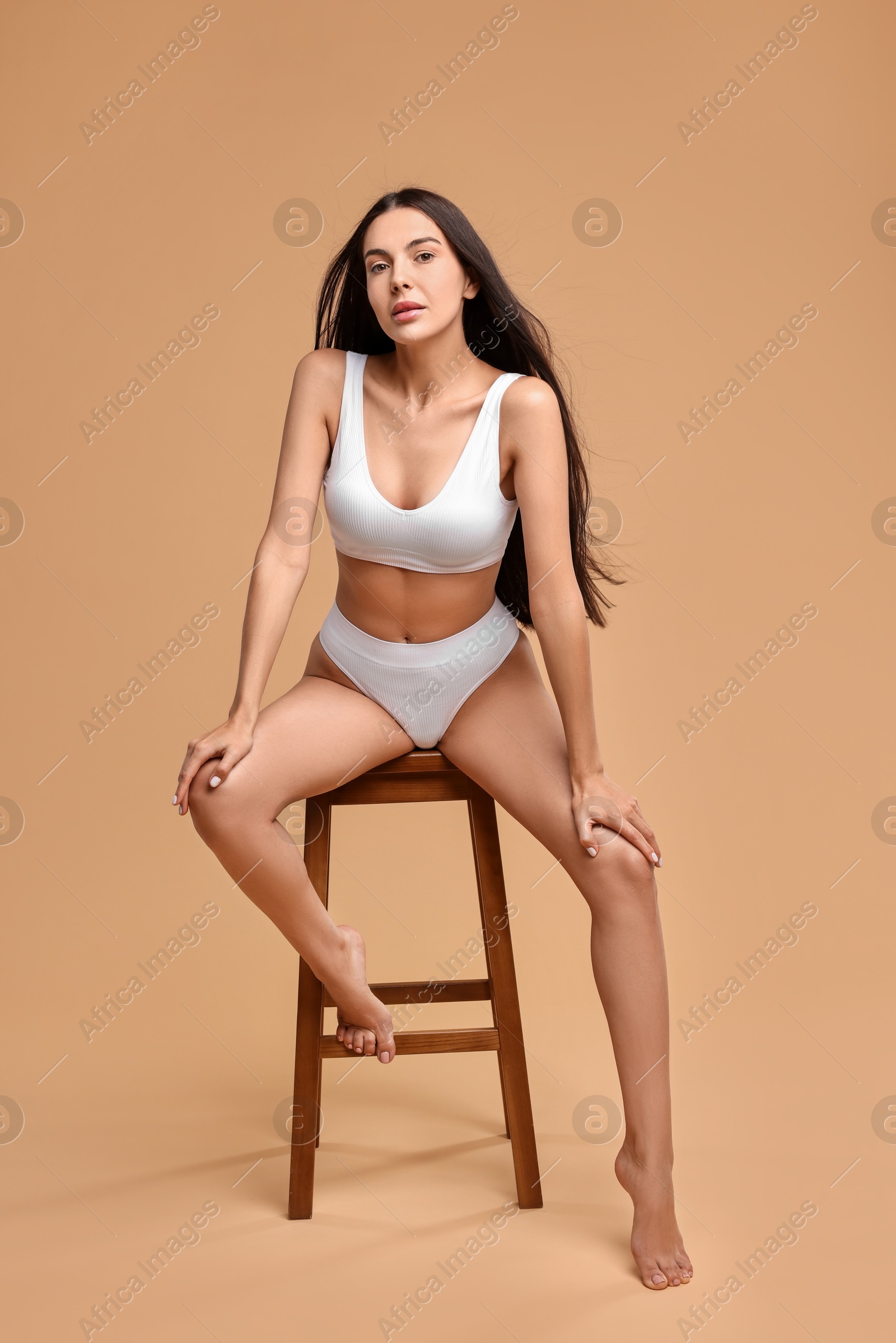 Photo of Beautiful woman with perfect skin in underwear posing on stool against beige background. Body care