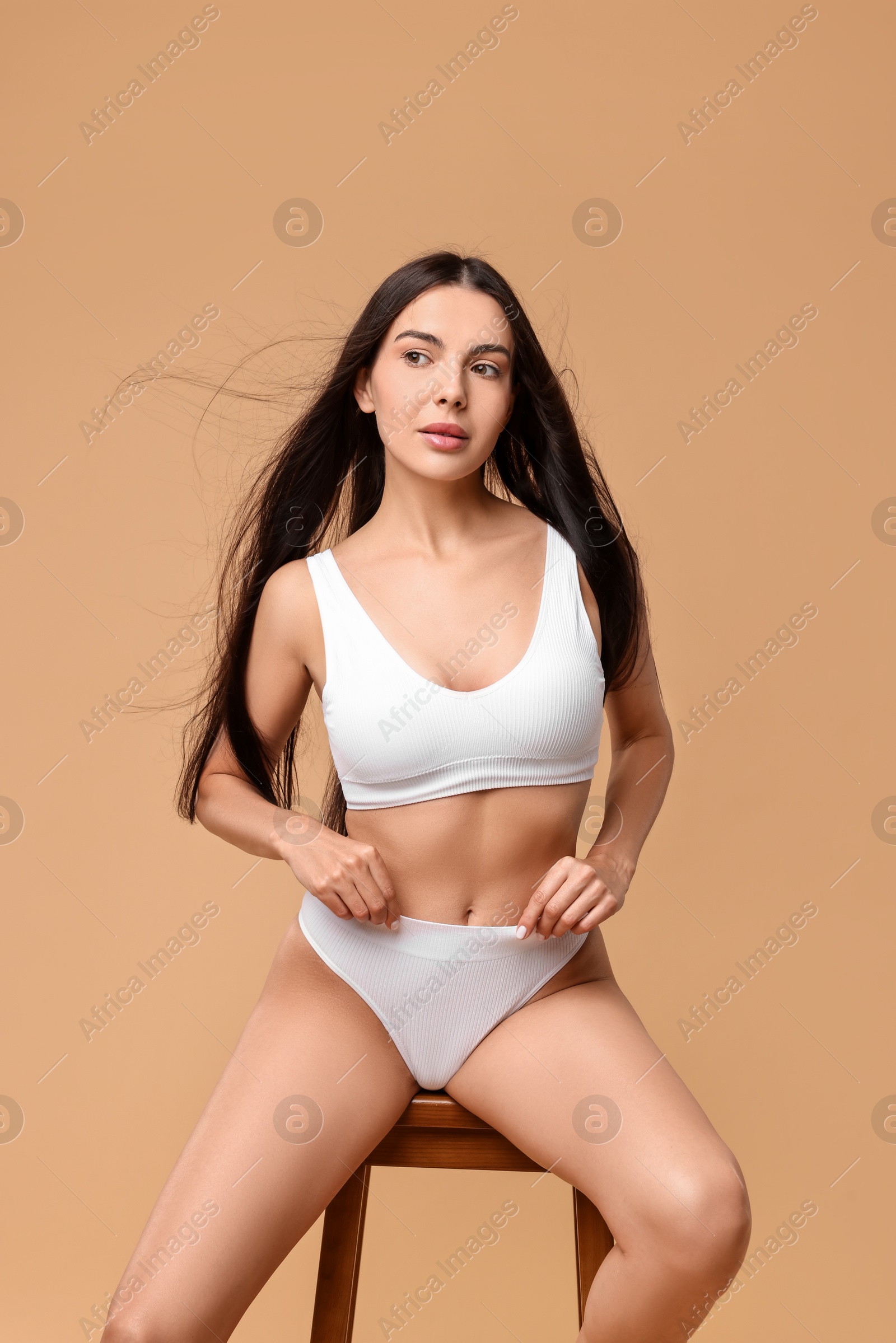 Photo of Beautiful woman with perfect skin in underwear posing on stool against beige background. Body care