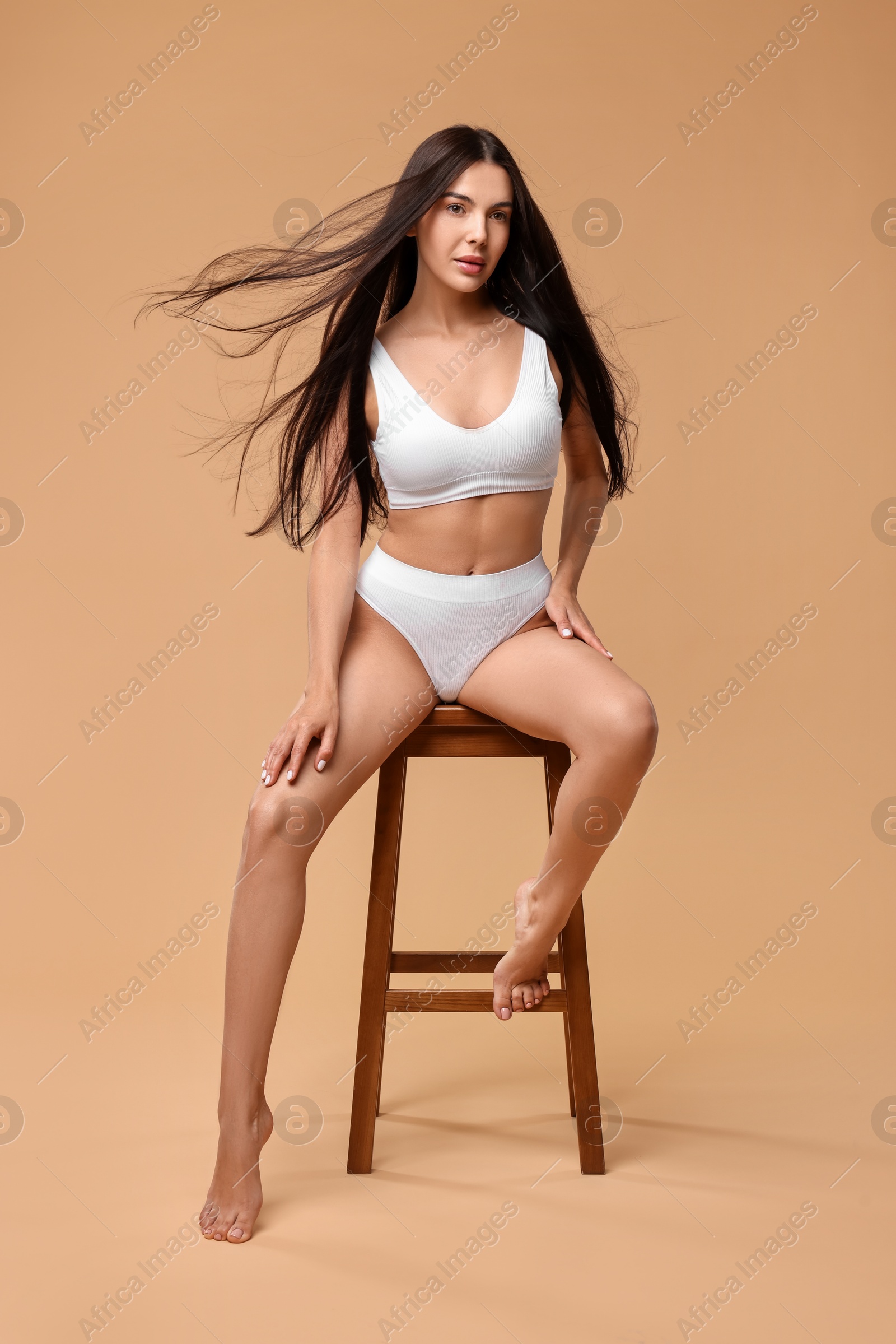 Photo of Beautiful woman with perfect skin in underwear posing on stool against beige background. Body care