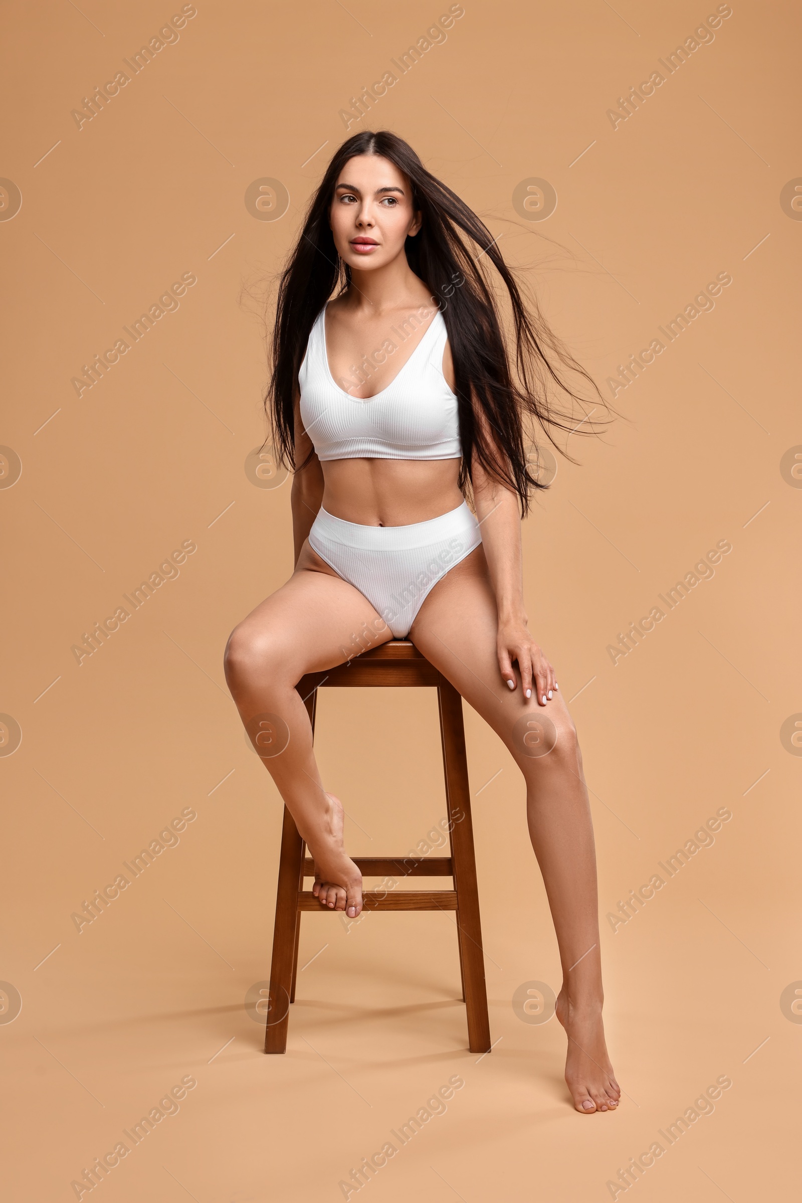 Photo of Beautiful woman with perfect skin in underwear posing on stool against beige background. Body care