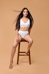 Photo of Beautiful woman with perfect skin in underwear posing on stool against beige background. Body care