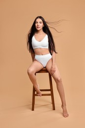 Photo of Beautiful woman with perfect skin in underwear posing on stool against beige background. Body care