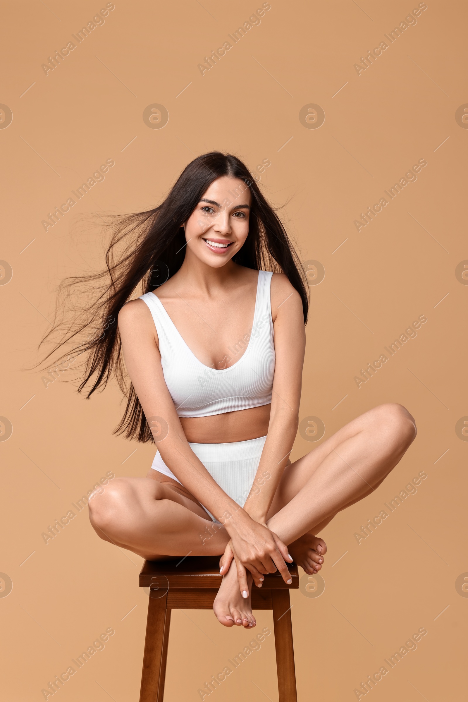 Photo of Smiling woman with perfect skin in underwear posing on stool against beige background. Body care