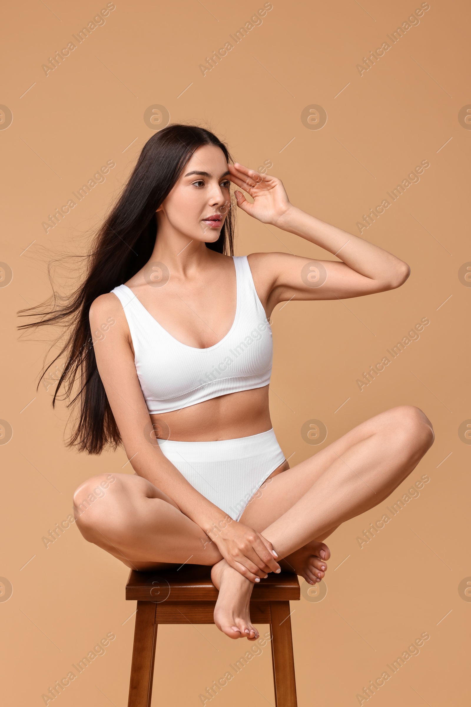 Photo of Beautiful woman with perfect skin in underwear posing on stool against beige background. Body care