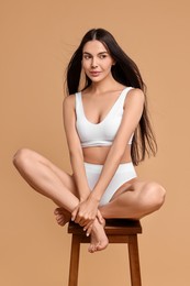 Photo of Beautiful woman with perfect skin in underwear posing on stool against beige background. Body care