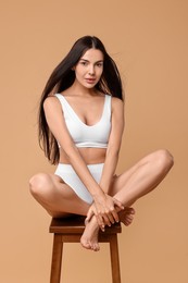 Beautiful woman with perfect skin in underwear posing on stool against beige background. Body care