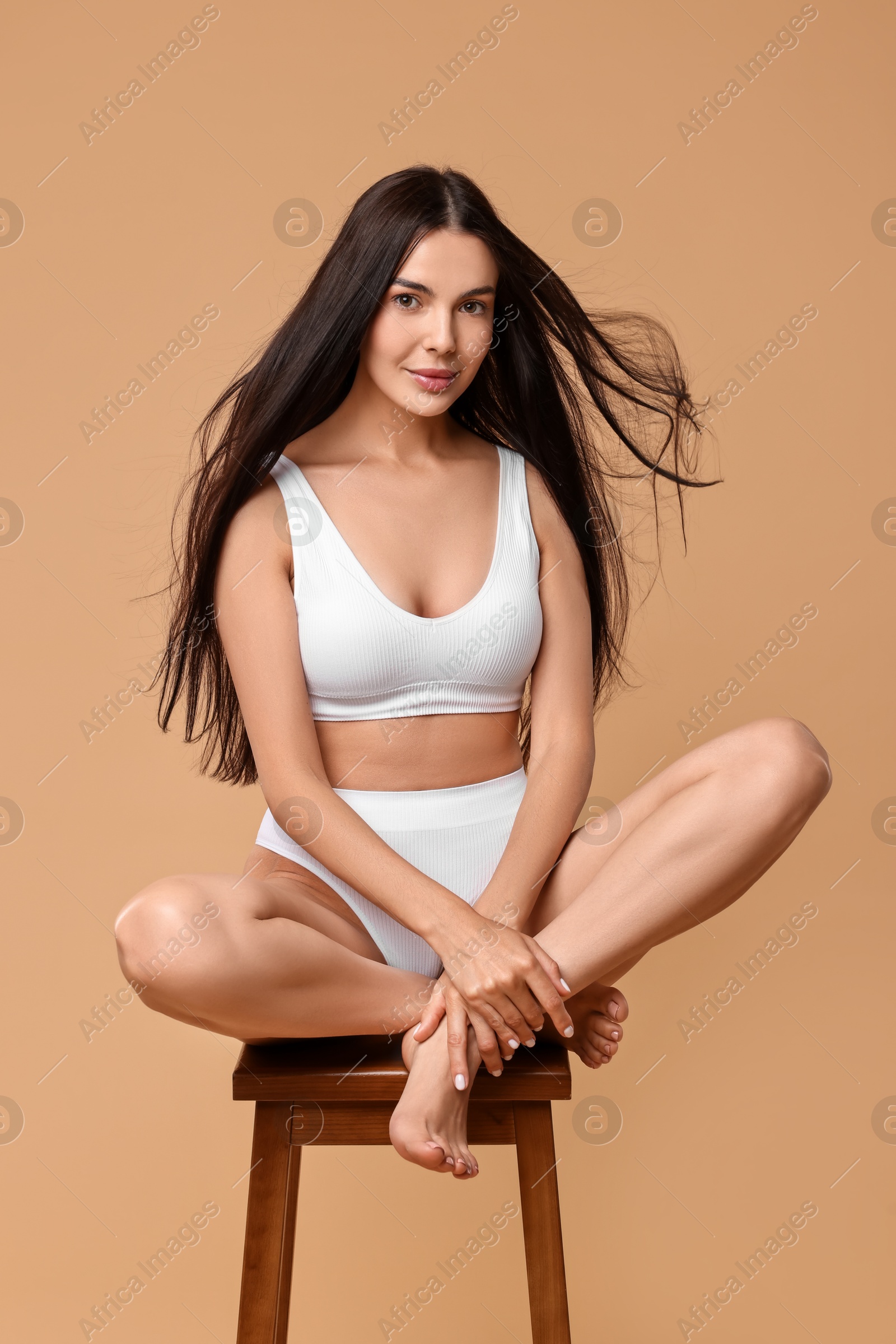 Photo of Beautiful woman with perfect skin in underwear posing on stool against beige background. Body care