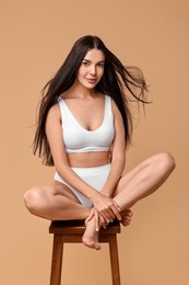 Photo of Beautiful woman with perfect skin in underwear posing on stool against beige background. Body care