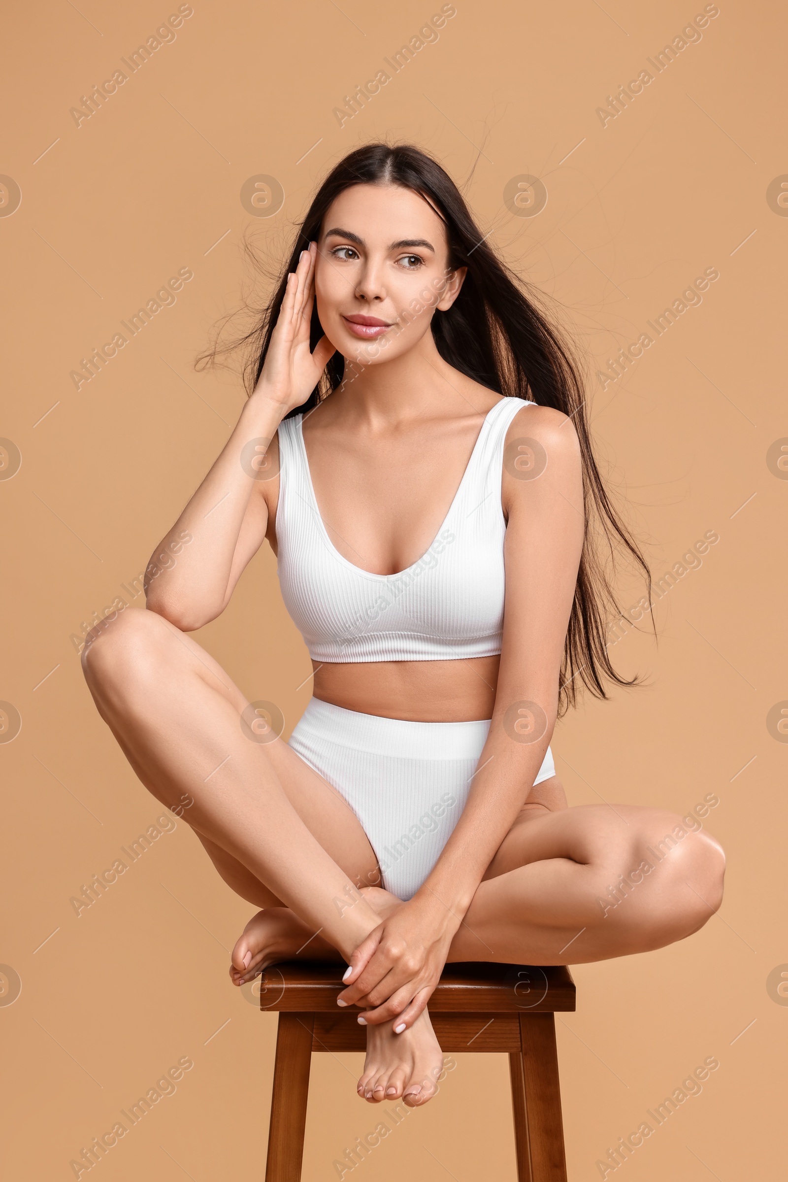 Photo of Beautiful woman with perfect skin in underwear posing on stool against beige background. Body care