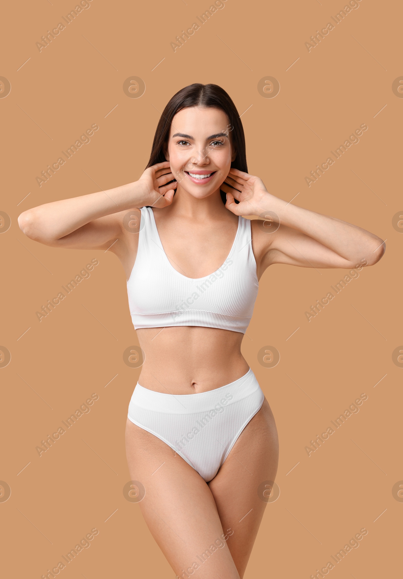 Photo of Smiling woman with perfect skin in underwear posing on beige background. Body care