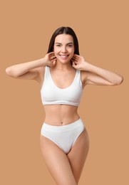 Smiling woman with perfect skin in underwear posing on beige background. Body care