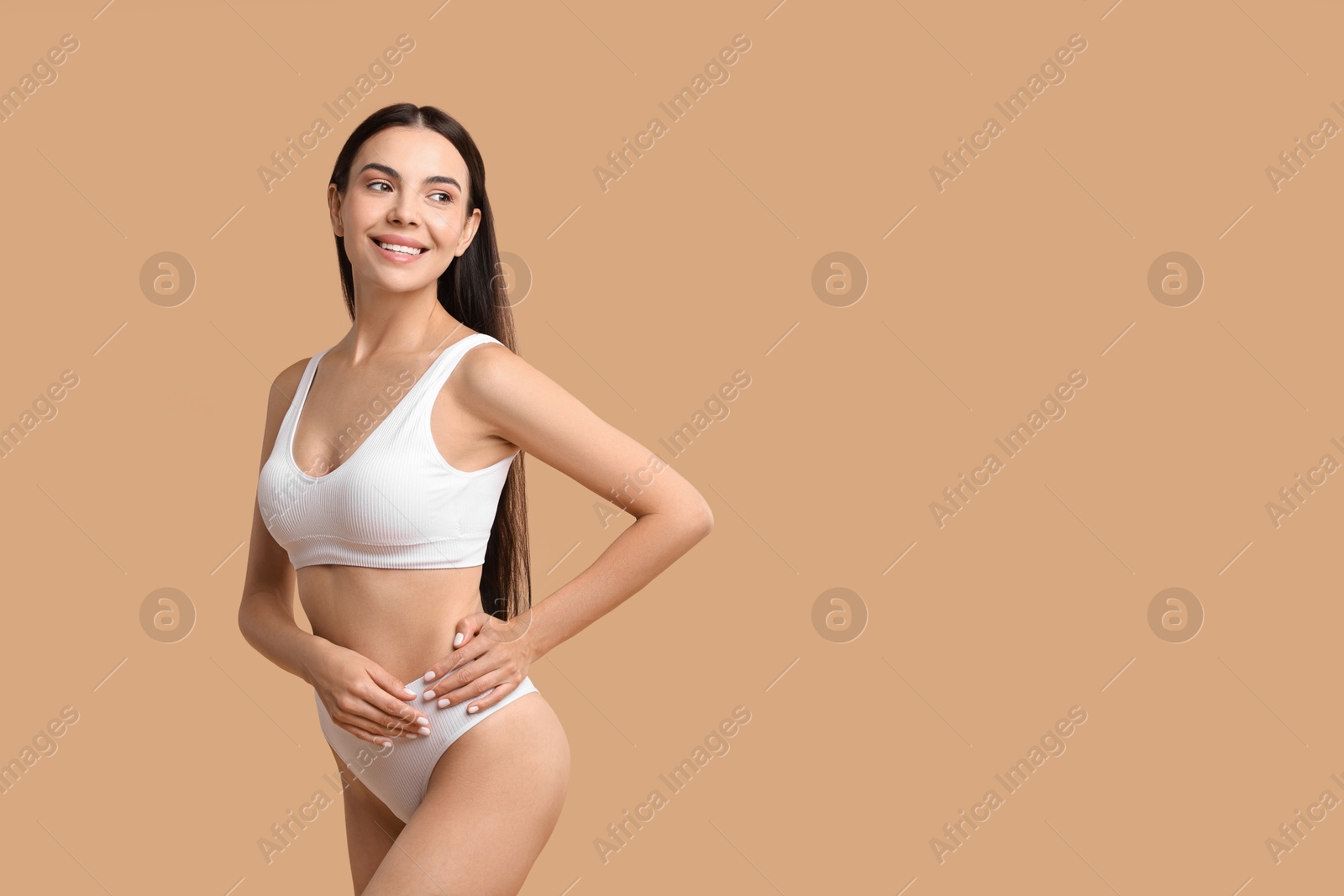 Photo of Smiling woman with perfect skin in underwear posing on beige background, space for text. Body care