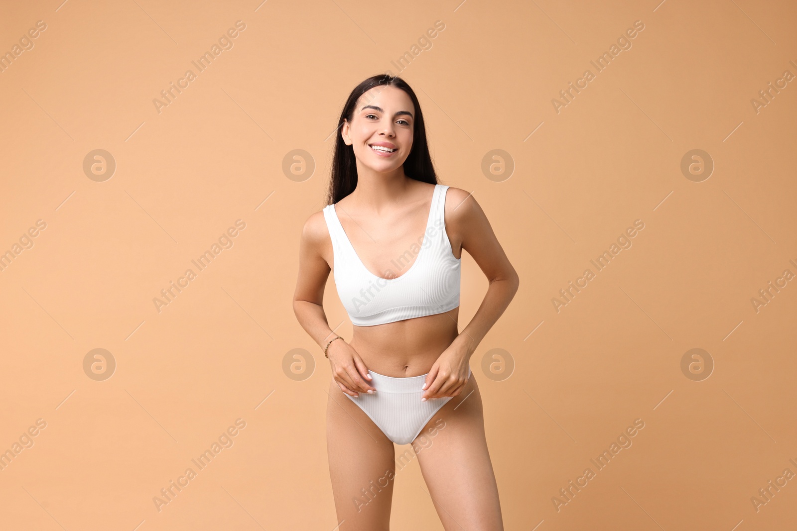 Photo of Smiling woman with perfect skin in underwear posing on beige background. Body care