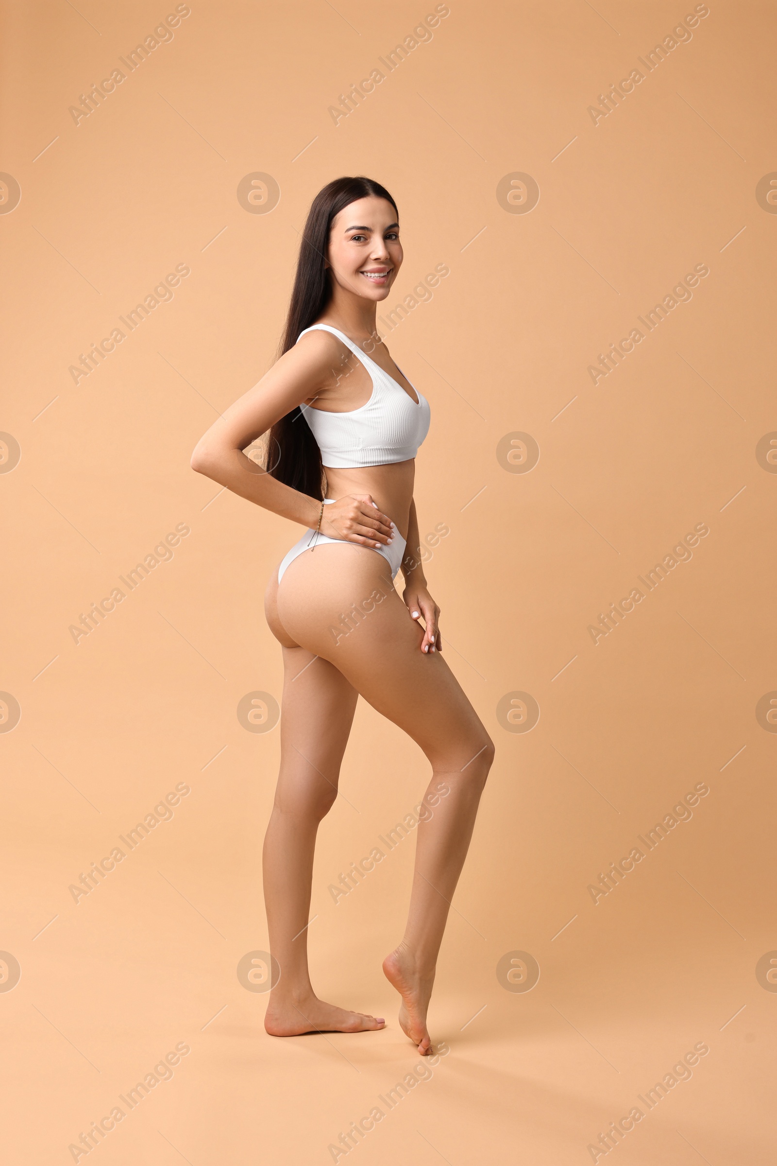 Photo of Smiling woman with perfect skin in underwear posing on beige background. Body care