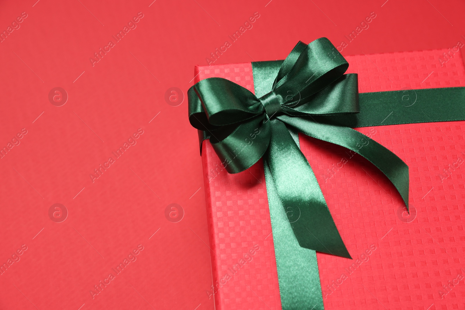 Photo of Gift box with green bow on red background, closeup. Space for text