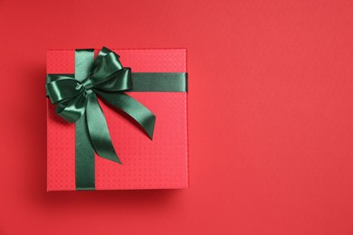 Photo of Gift box with green bow on red background, top view. Space for text