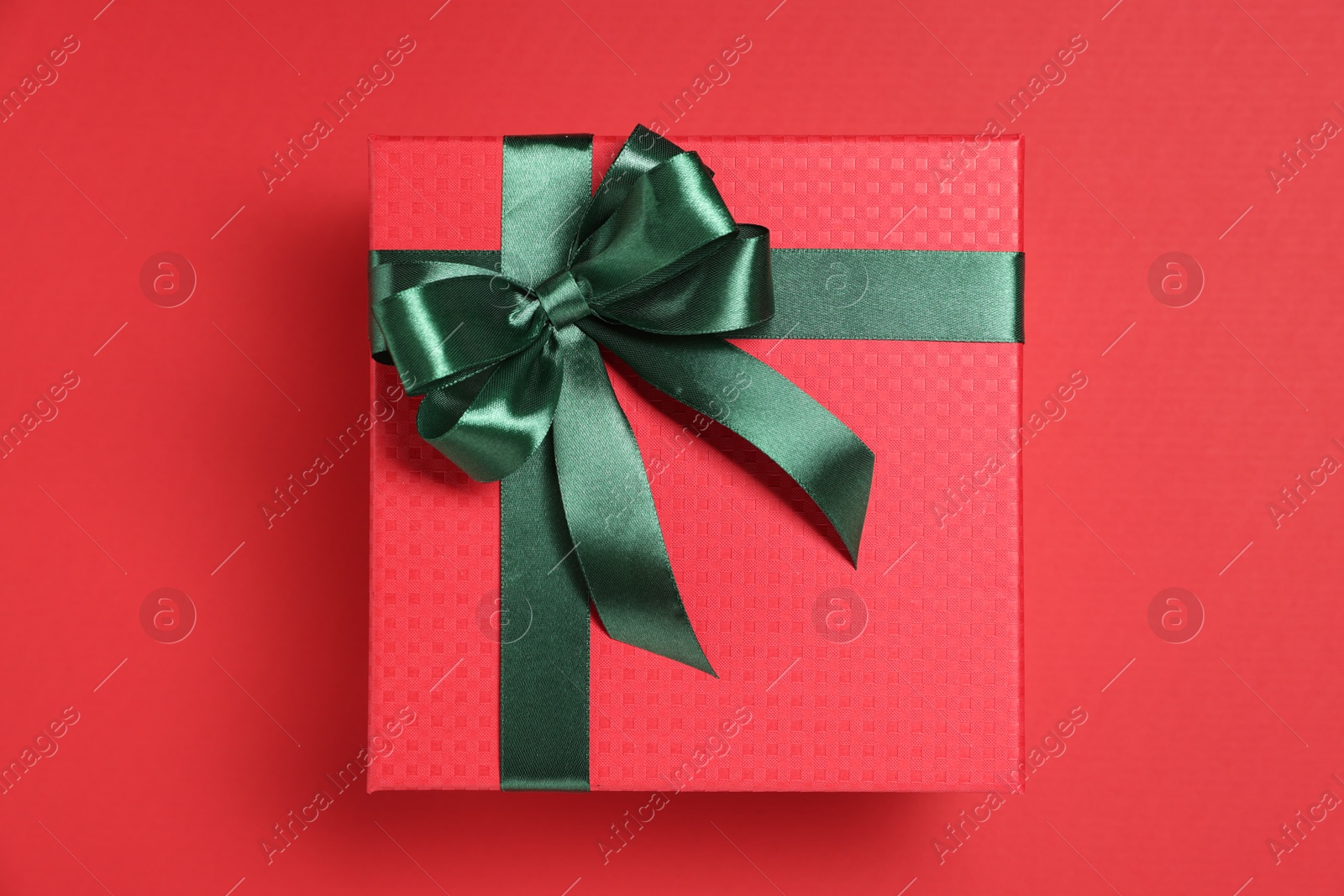 Photo of Gift box with green bow on red background, top view