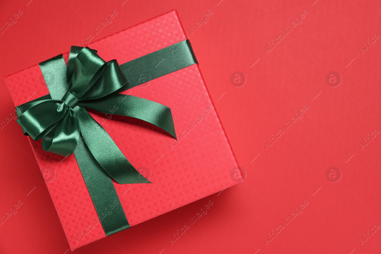 Photo of Gift box with green bow on red background, top view. Space for text