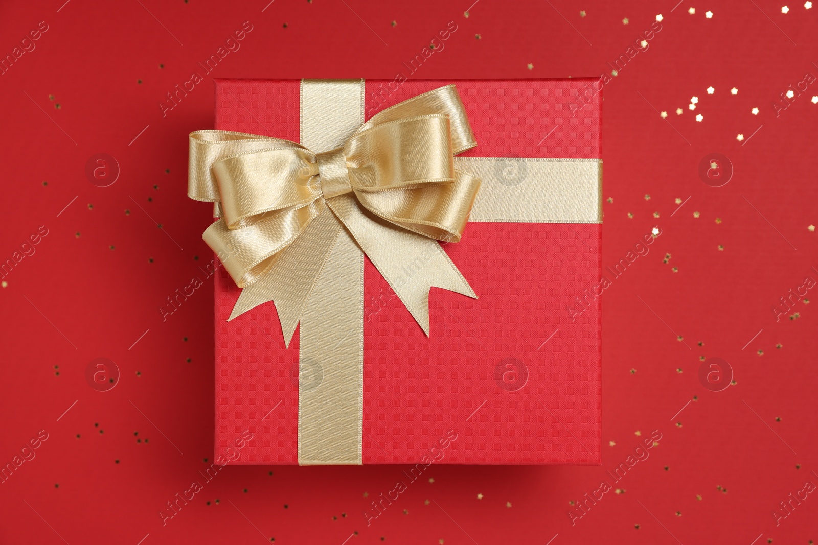 Photo of Gift box with bow and confetti on red background, top view