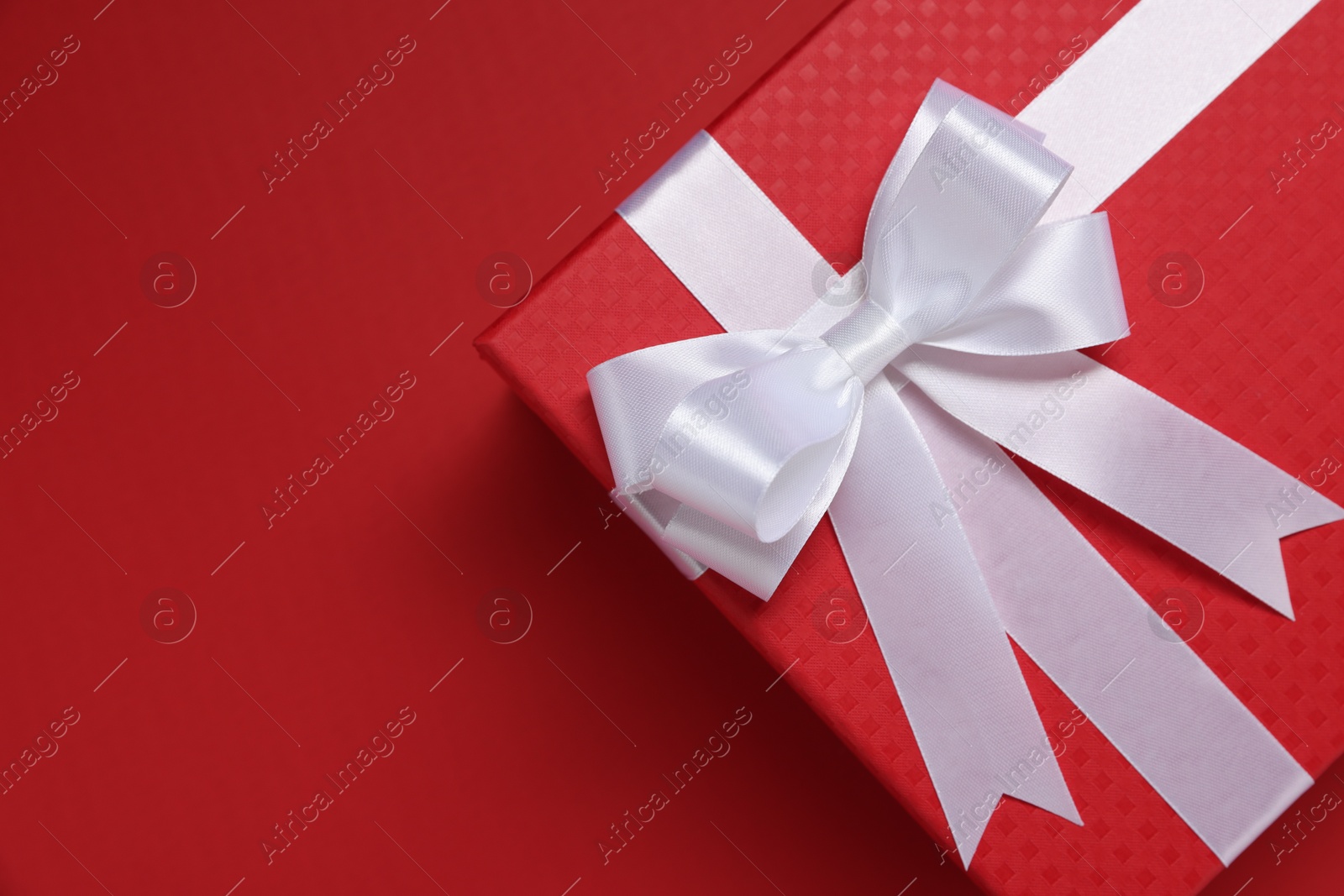 Photo of Gift box with white bow on red background, top view. Space for text