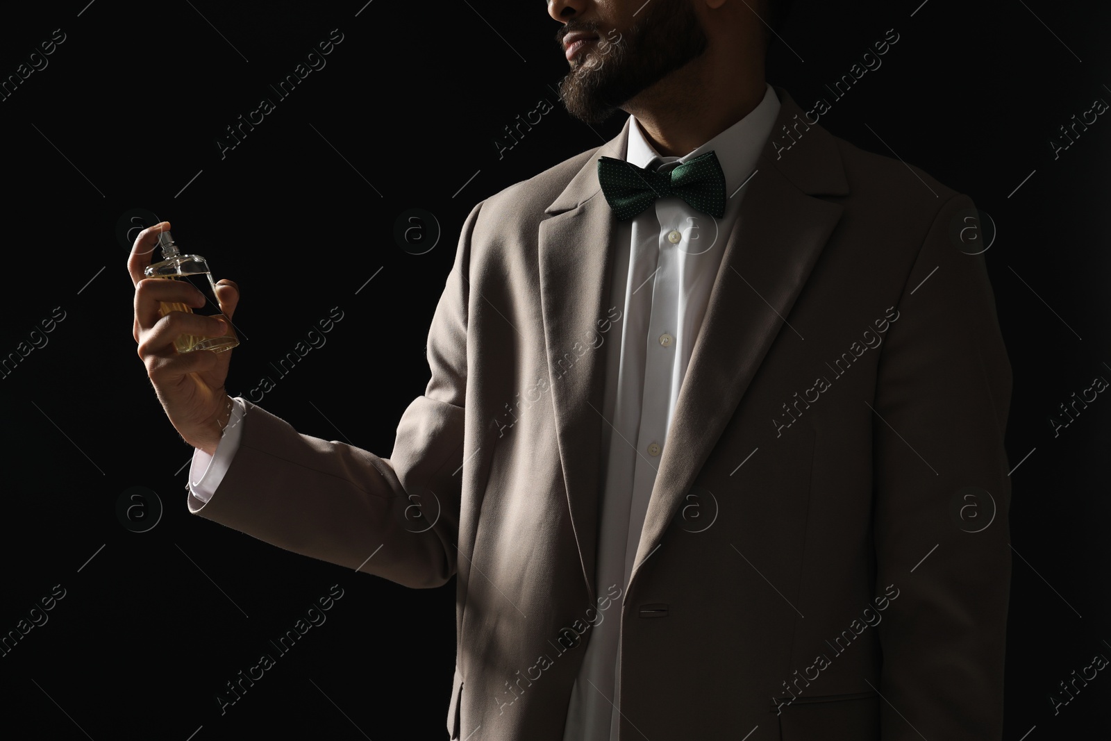 Photo of Man spraying luxury perfume on dark background, closeup