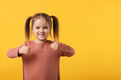 Photo of Cute little girl showing thumbs up on orange background, space for text