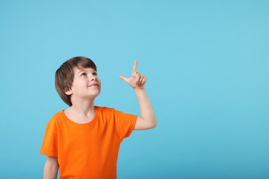 Photo of Cute little boy pointing at something on light blue background, space for text