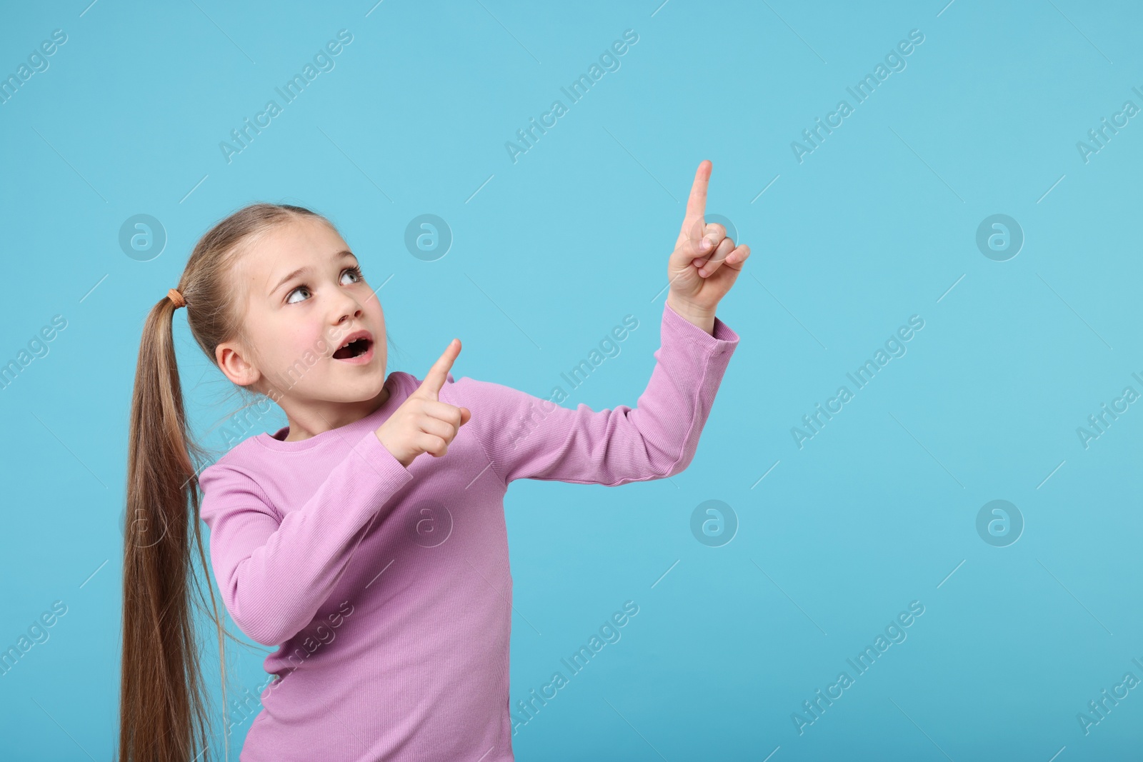 Photo of Cute little girl pointing at something on light blue background, space for text
