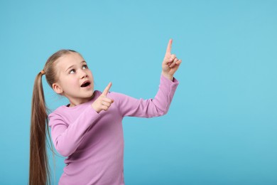 Photo of Cute little girl pointing at something on light blue background, space for text