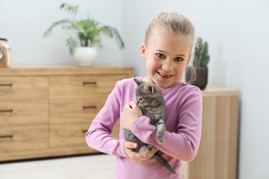 Photo of Little girl with cute fluffy kitten indoors, space for text