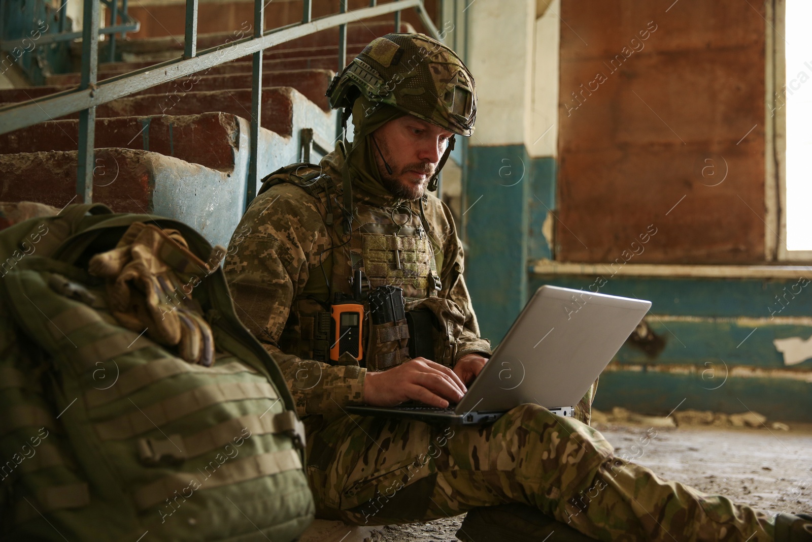 Photo of Military mission. Soldier in uniform using laptop inside abandoned building