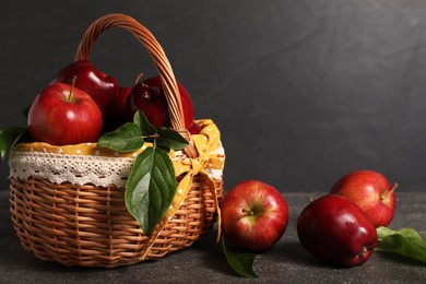 Ripe red apples and leaves in wicker basket on dark grey table. Space for text